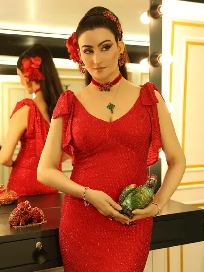A close-up on the details. The look was accessorized with a red floral choker, a cross pendant, and a unique parrot-shaped clutch by Judith Leiber, adding a touch of playful luxury to the overall ensemble.