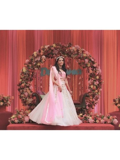 Our virtual bride looking radiant at her engagement ceremony. We styled this elegant white and pink lehenga look for her, complete with a floral backdrop that we coordinated with her outfit's color palette.