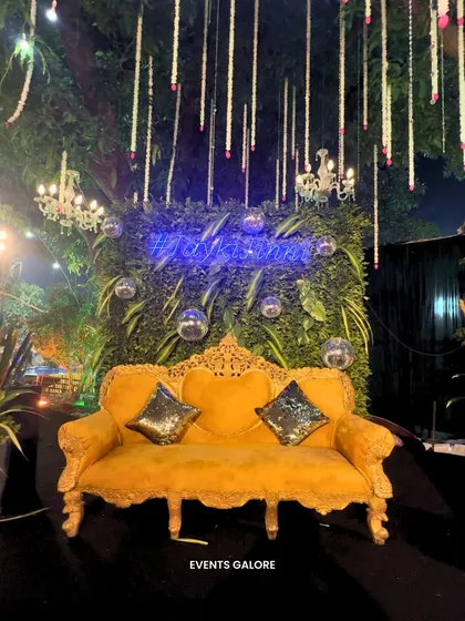 A chic photo spot with a vintage yellow sofa set against a green wall with a neon sign. Details like disco balls and hanging florals add to the glamorous vibe.