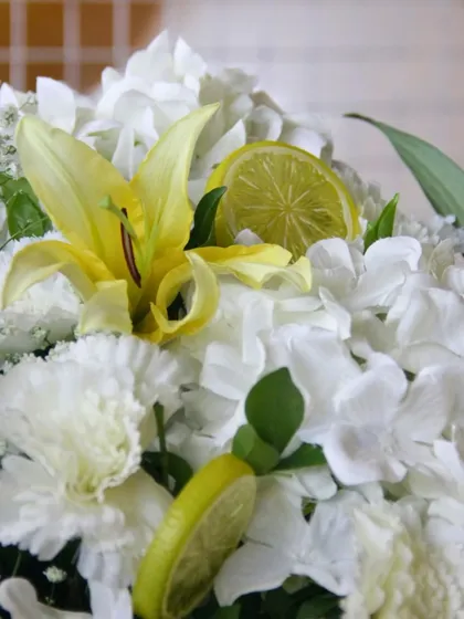A macro shot of a floral arrangement featuring white hydrangeas, yellow lilies, and a slice of lemon, perfectly capturing the fresh, zesty theme.