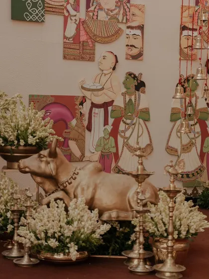 A decor corner featuring a brass Nandi statue, traditional lamps (diyas), and arrangements of white tuberoses, all set against a backdrop of Indian folk art. This is a perfect blend of tradition and aesthetics.