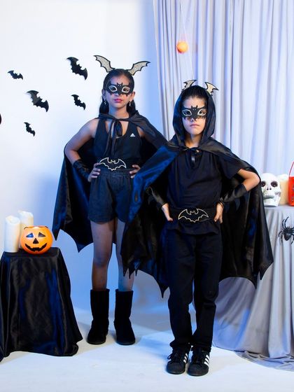 Two children in matching bat-themed Halloween costumes.
