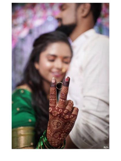 A creative engagement photo, with the bride's hand and ring in focus, making a victory sign.