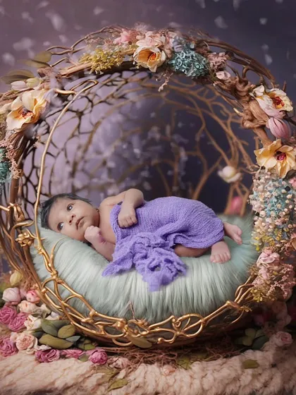 An awake newborn wrapped in purple, looking up from an ornate, nest-like golden prop.