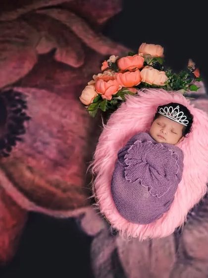 Every baby is a little princess. This shot features a newborn wearing a tiny tiara, nestled in a pink fur-lined basket against a dramatic floral background.