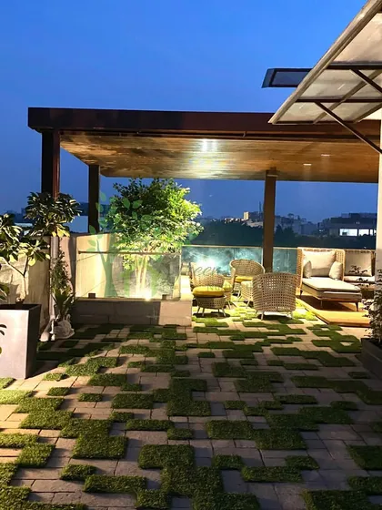 This is a photograph of a completed rooftop project at dusk. The combination of a wooden pergola, soft lighting, and unique checkerboard turf flooring demonstrates our ability to turn design concepts into beautiful, functional realities.