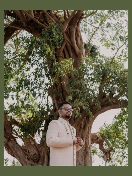 A stylish portrait of the groom, Rahul, standing under a large tree, looking cool and composed before his wedding.