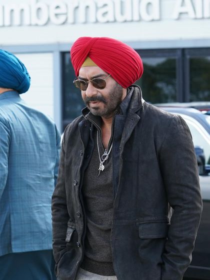 This on-set photo shows Jassi's layered, rugged style for the Scotland schedule. He wears a dark jacket over a tonal sweater, paired with a bold red turban. The look is practical for the setting yet maintains the character's signature sharp and stylish aesthetic.