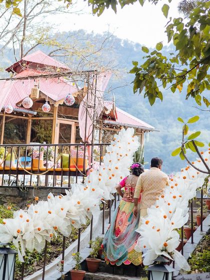 The couple walking down a path at their Corbett venue, with the beautiful Mehendi decor in the background.