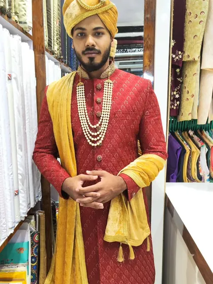 Nothing commands attention like a classic red sherwani. This groom is ready for his big day in a rich red brocade sherwani, perfectly accessorized with a golden pagdi and a traditional pearl necklace.