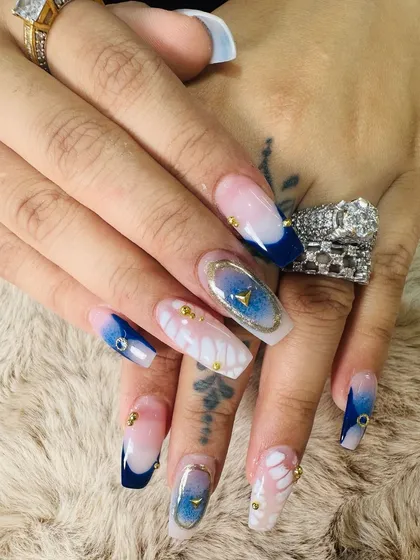 Let's get creative with mixed media. This design combines a deep blue french tip, delicate floral patterns, and encapsulated gold elements for a truly unique, dimensional look.