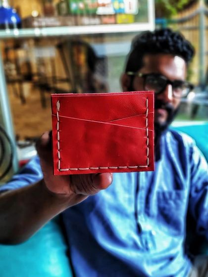 An artist proudly presenting a bright red, hand-stitched leather cardholder. Our workshops encourage you to experiment with different colors and designs to create a piece that reflects your personal style.