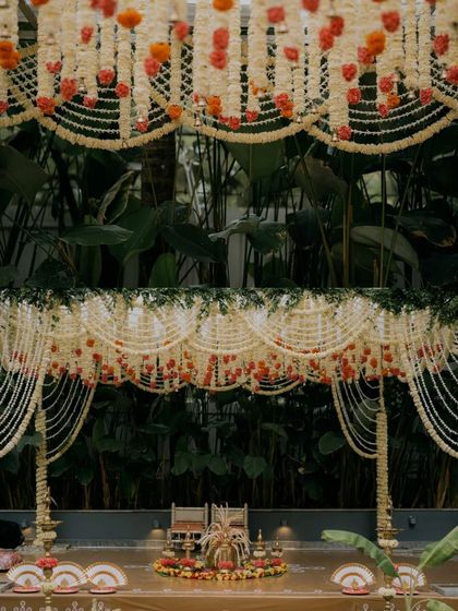 A full view of a stunning mandap decorated with intricate curtains of tuberose and marigolds, set against a backdrop of lush tropical leaves. The design is both traditional and fresh.