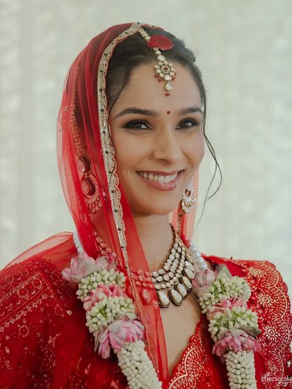 A classic bridal portrait, smiling and looking directly at the camera, radiant in her red lehenga.
