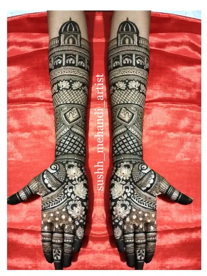 This grand bridal mehandi features palace domes on the arms and intricate floral and peacock work on the hands, all against a striking red background.