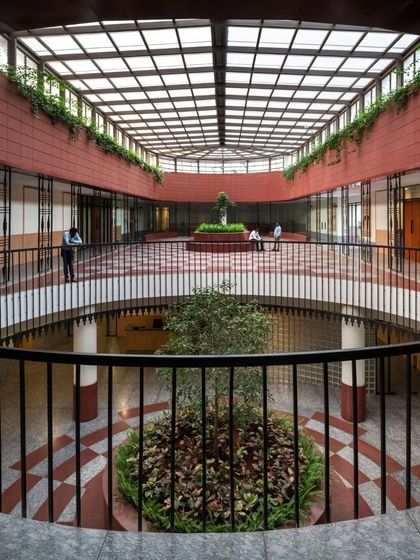 A large, sky-lit central atrium brings natural light deep into the building and connects the different floors, with trees planted on multiple levels.