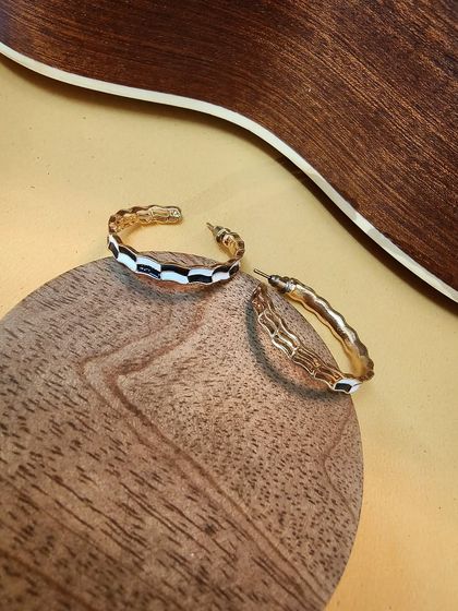 A product shot of the non-tarnish black and white enamel hoop earrings, resting on a wooden surface.