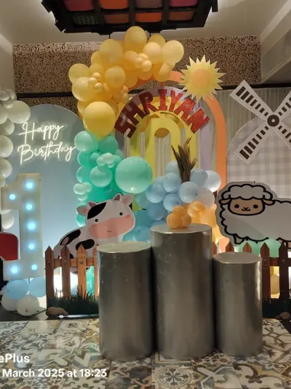 We brought the countryside to the city with this farm-themed first birthday. The setup includes a tractor cutout, a windmill prop, cute farm animal characters, and a "1" marquee number against a backdrop of soft-colored balloons.