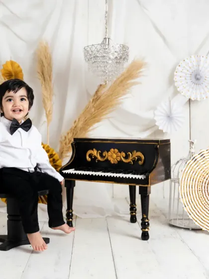 A dapper little gentleman dressed in a bow tie for his 'Pianist' themed session. He poses with a miniature piano, creating a classic and charming toddler portrait.