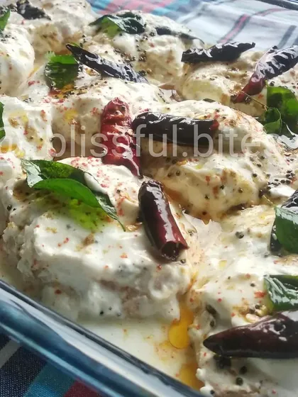 A close-up of my homemade Dahi Vade, a classic and refreshing chaat. Soft lentil fritters are soaked in creamy, spiced yogurt and garnished with a tempering of curry leaves and dried red chilies for a burst of flavor.