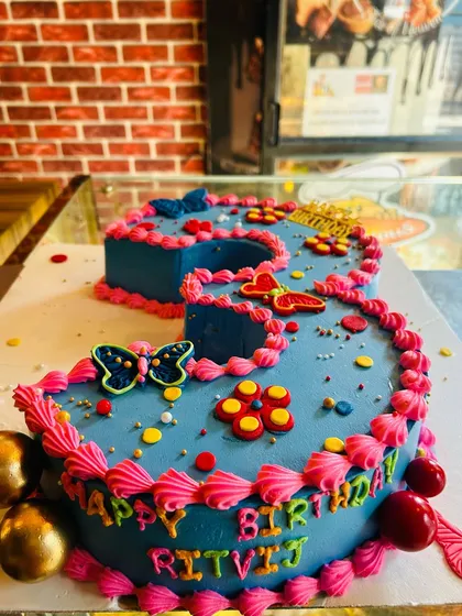A bright and colorful number "3" shaped cake, decorated with pink piping and edible butterflies.
