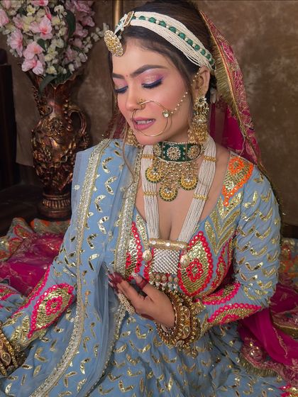 This shot highlights the detailed craftsmanship of the blouse and the heavy bridal jewellery. The nath, matha patti, and layered necklaces are all available for rent to complete your look.