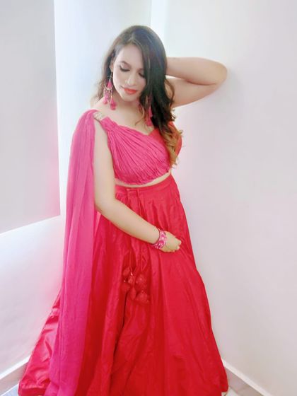 A happy client wearing a custom-designed red lehenga with a modern draped blouse. The one-shoulder cape adds a contemporary twist to the traditional lehenga choli.