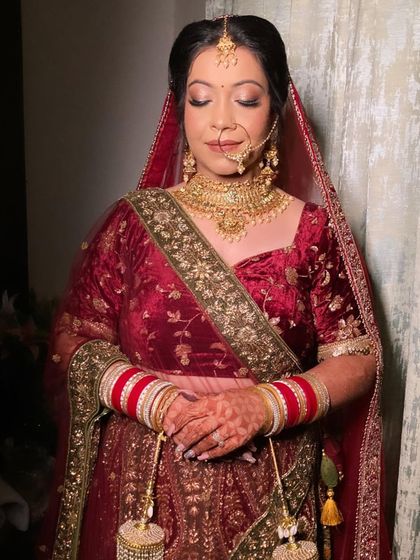 A full portrait showing the complete bridal look. The velvet lehenga and gold jewelry are perfectly complemented by the warm, glowing makeup.