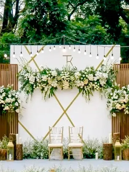 This rustic-chic reception backdrop features a monogrammed white panel accented with wooden slats and beautiful white floral arrangements. The warm Edison bulbs add a touch of vintage charm.