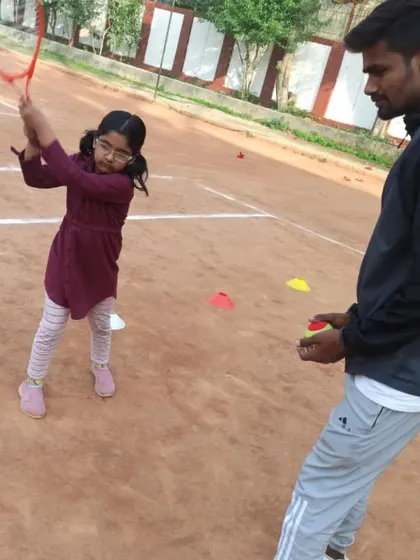 A young girl practicing her swing with the coach observing closely. Her high racket preparation is a good sign of proper technique.