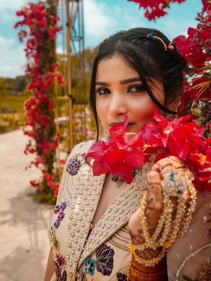 A close-up of our client's Mehendi look, framed by beautiful red flowers. The golden pearl hand harness adds a touch of warmth and elegance to her overall style.