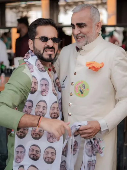 A fun, candid moment from the baraat, with a guest wearing a custom scarf featuring the groom's face.