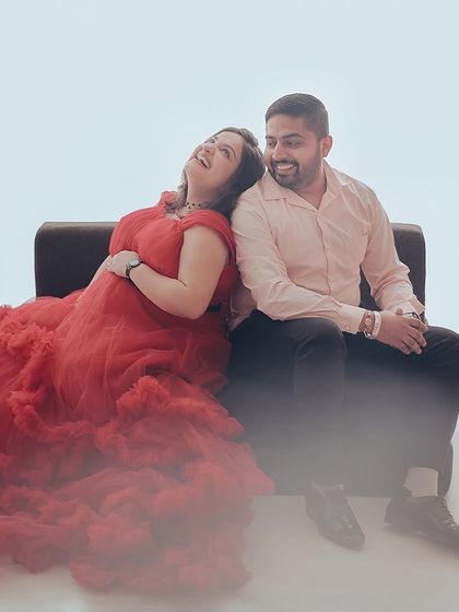 Another angle of a happy couple's shoot, with the mom-to-be in a vibrant red ruffled gown. The soft lighting highlights the joy and connection between the couple.