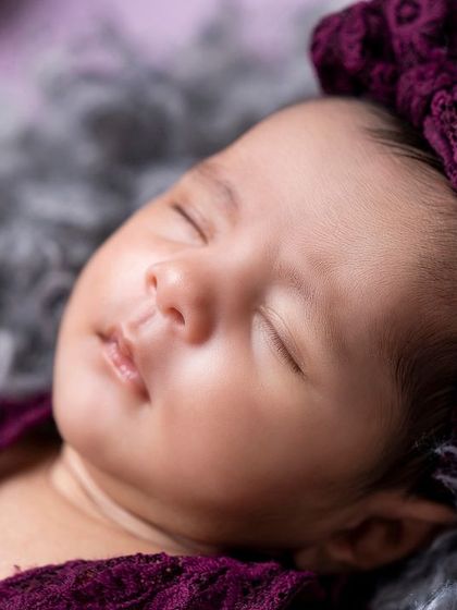 A close-up of a sleeping newborn in a rich purple outfit, highlighting her perfect, delicate features.