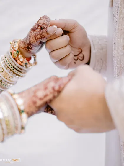 A close-up of the couple holding hands, showcasing the intricate mehendi and the simple, powerful gesture of their connection.