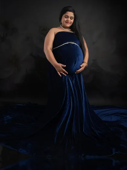 A classic maternity portrait in a luxurious royal blue velvet gown. The fabric drapes beautifully, and the soft lighting creates a serene and elegant mood.