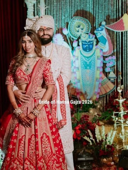 A full-length portrait of the couple in a traditional setting. The bride's mehendi is a beautiful part of her overall red bridal look, adding to the richness and grandeur.