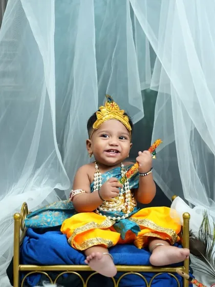 A happy little Krishna, smiling and holding his flute. The sheer white curtain in the background adds a touch of softness and elegance to the setup.