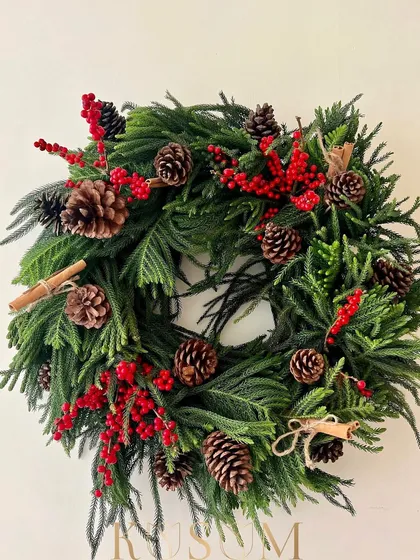 The charming Christmas wreath. This design is full of texture, with fresh pine, bright red ilex berries, pinecones, and cinnamon sticks. It can be hung on a door or laid flat with a candle in the middle.