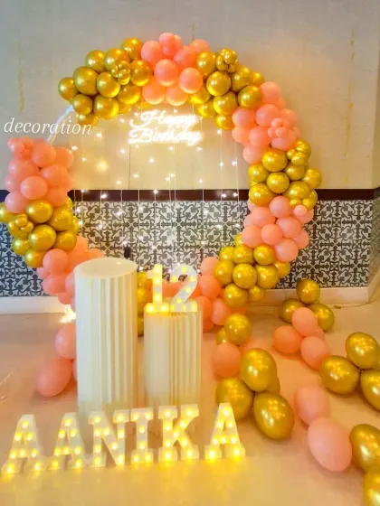 A stylish birthday setup for a 12-year-old using a circular balloon arch in peach and gold. The decor includes a neon sign, marquee number, and personalized name.