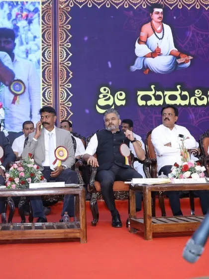 Seated on the dais with other dignitaries during the Siddharameshwara Jayanti event. My image is also visible on the large screen behind the stage.