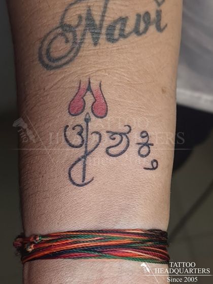 A small tattoo on the wrist in Kannada script, "Om Shakti," invoking divine energy, placed just above a colorful wristband.