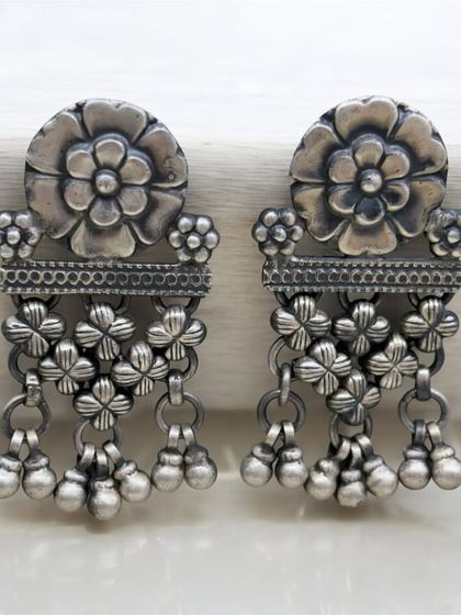 Elegant and stunning silver oxidised earrings. This pair features a floral top and a drop made of smaller, linked floral charms with ghungroos.