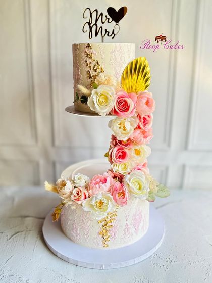 A modern design for a Mr. & Mrs. This unique S-shaped floating cake features two separate tiers connected by a cascade of pink and white roses, creating a stunning visual effect for a wedding or reception.