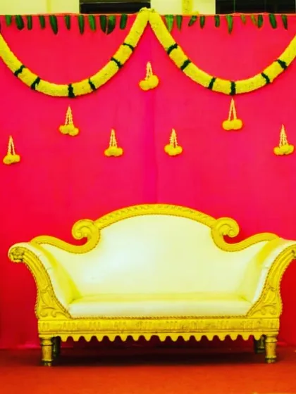 A simple stage setup with a bright pink backdrop and marigold garlands. The elegant white and gold sofa completes this classic look for a baby shower.