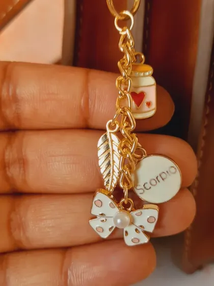 A close-up of a custom bag charm for a Scorpio, featuring a polka-dot bow, a leaf charm, a love potion bottle, and the Scorpio zodiac sign.
