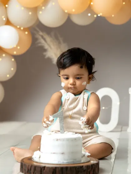 A moment of intense focus on the cake. Dressed in adorable overalls, this little one is ready to dive into his first birthday celebration.