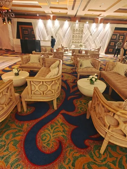 Plush, intricately carved wooden lounge seating arranged for guest comfort at a large reception, allowing for conversation while still having a view of the main stage.