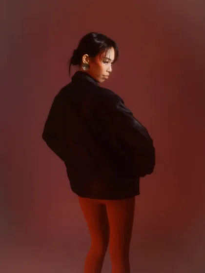A moody shot for a fashion editorial. The makeup is minimal with a pop of red blush, paired with a sleek, wet-look bun to create an edgy, modern vibe.