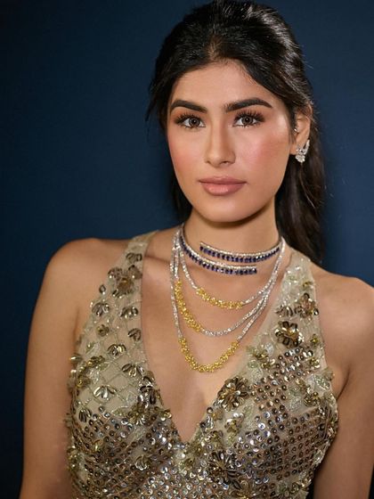 A close-up of the glamorous evening look. The makeup is soft and natural, with a focus on a healthy glow and defined brows, allowing the layered necklaces to make a statement.